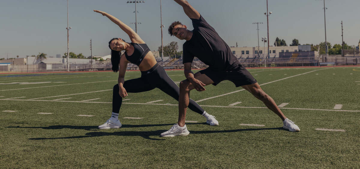 Two people stretching on a sports field, from ALO Wellness Club's student page.